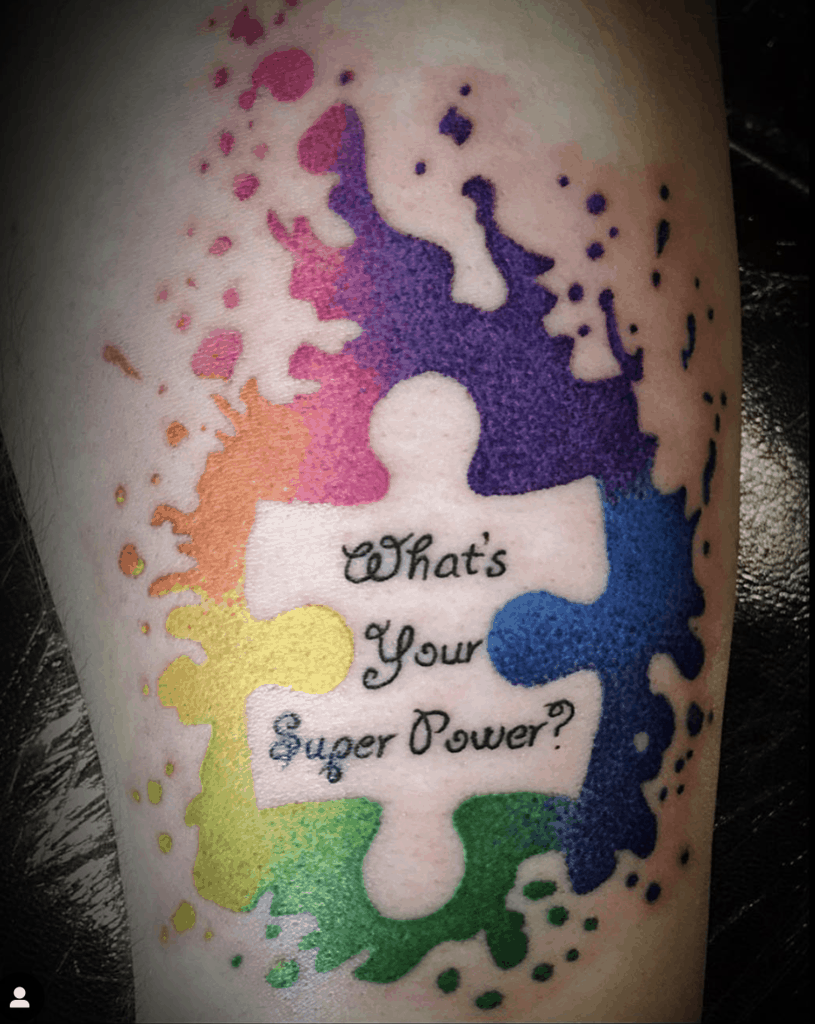 Full color tattoo of watercolor splashes and negative space puzzle piece with an inspirational quote.