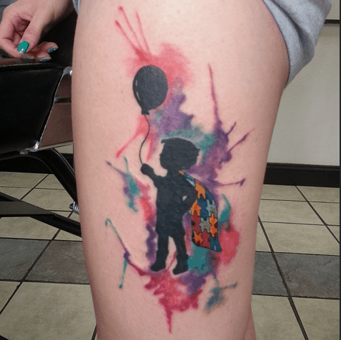 Full color thigh tattoo of child’s silhouette with balloon and puzzle piece cape with watercolor splashes.