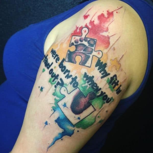Full color upper-arm tattoo of puzzle pieces with baby foot print, watercolor splashes and inspirational quote.