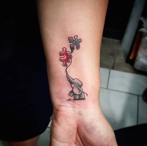 Full color wrist tattoo of a baby elephant holding two puzzle piece balloons.