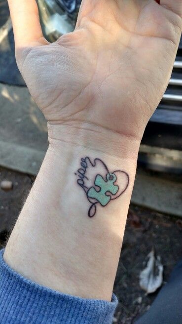 Full color wrist tattoo of a puzzle piece with a string that forms a heart and “piper”.