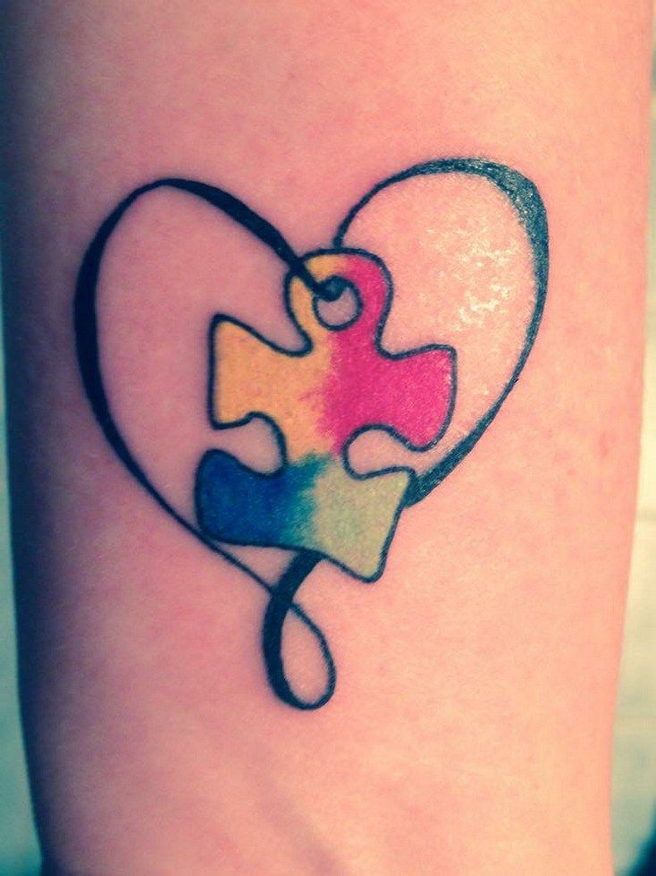 Full color wrist tattoo of a thing black heart with a multi-colored puzzle piece suspended inside. 