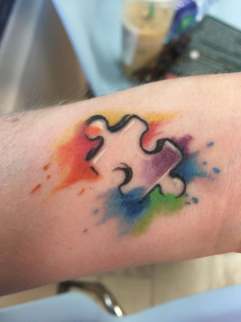 Full color wrist tattoo of line work puzzle piece with watercolor splashes.