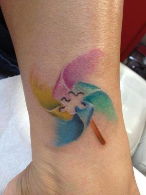Full color wrist tattoo of watercolor pinwheel with negative space puzzle piece.