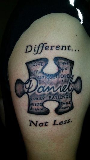 Large black and gray thigh tattoo of a puzzle piece with “Daniel” and inspirational quotes.