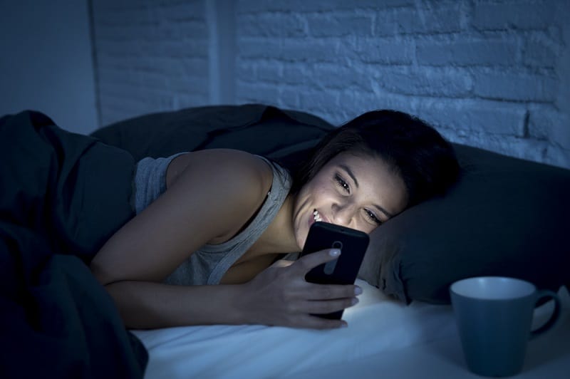 Woman Smiling Looking At Phone In Bed