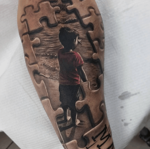 Limited color forearm tattoo of puzzle pieces with missing pieces revealing a realistic child at the beach.