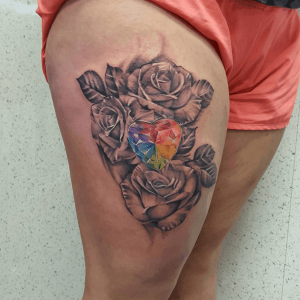 Limited color thigh tattoo of black and gray roses surrounding a multi-colored gem stone heart.