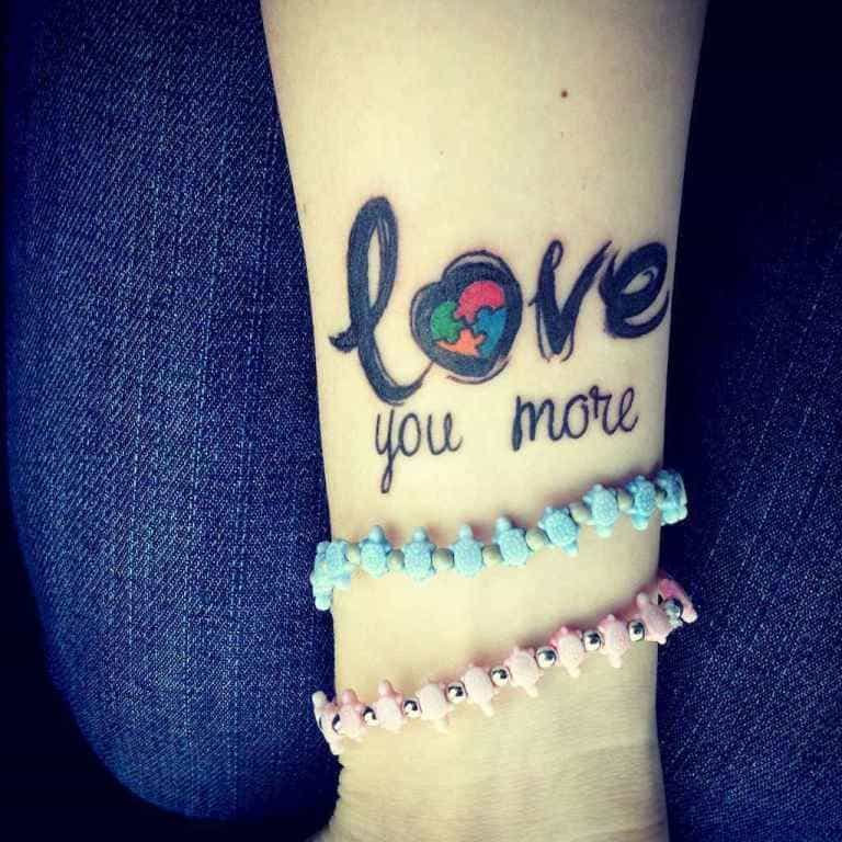 Limited color wrist tattoo of “Love you more” with puzzle pieces filling the heart-shaped “O”.