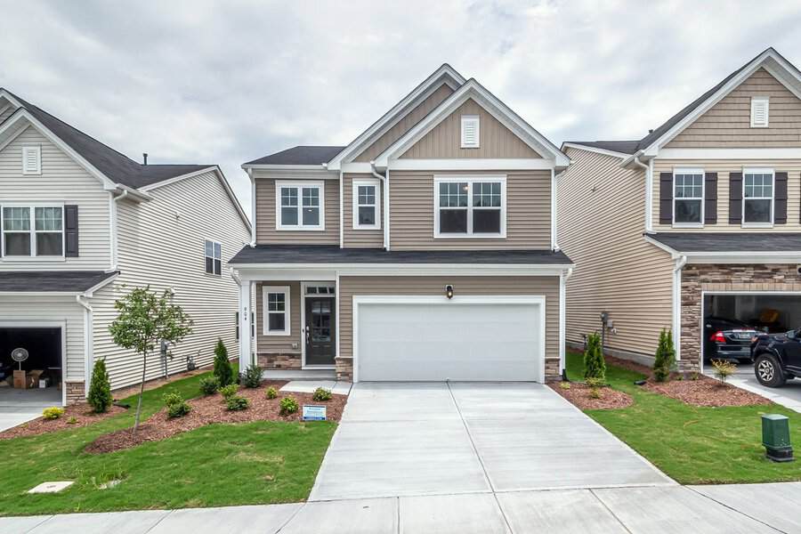 Two-story suburban house with beige siding, white trim, double garage, and neat landscaping—great curb appeal
