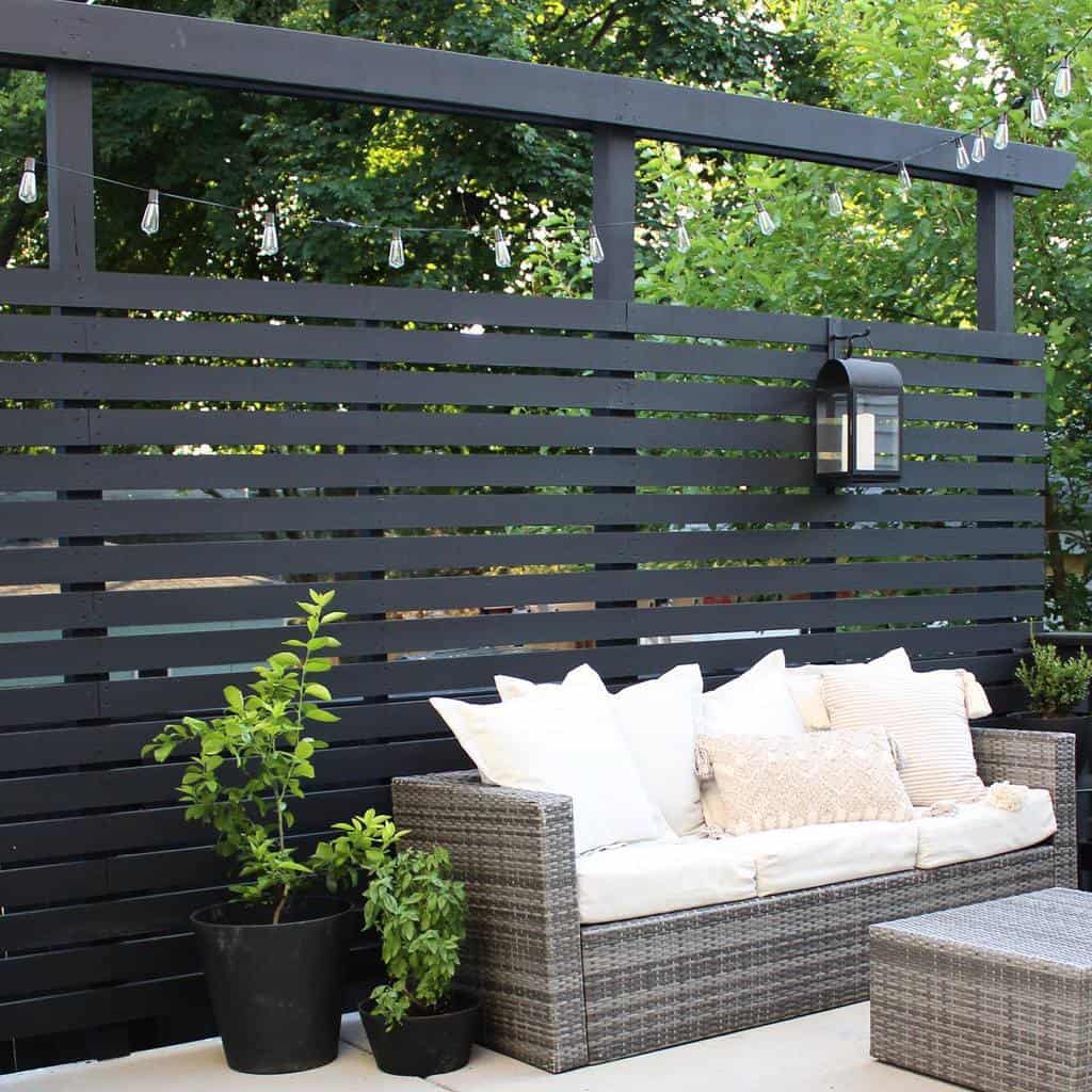 backyard patio black wood panel fence gray wicker sofa pot plants