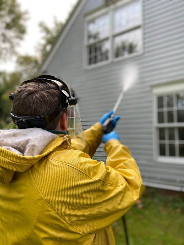 Person in yellow raincoat and face shield pressure washing siding with a spray wand for instant curb appeal
