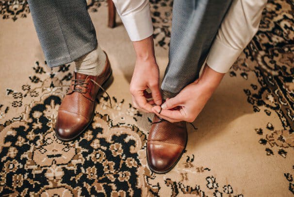 Tying a brown pair of dress shoes on a floral rug