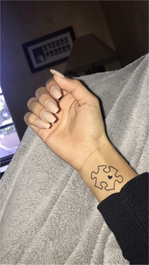 Simple line work puzzle piece tattoo with a small heart on the wrist.