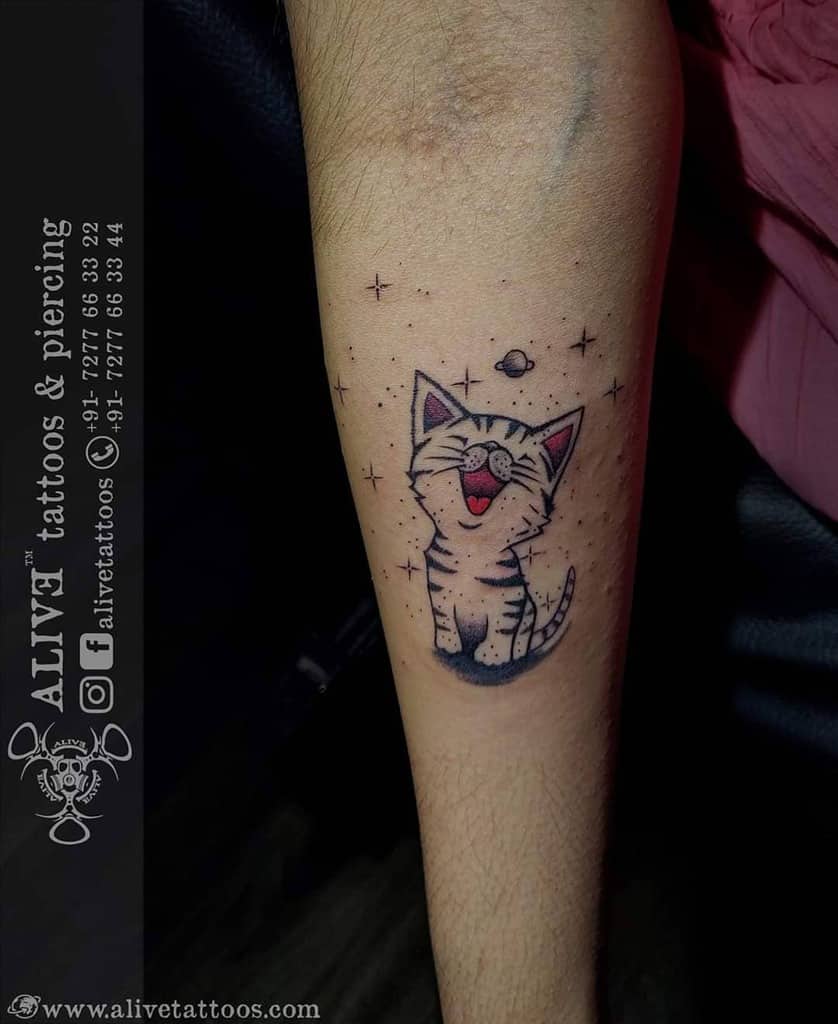 Tattoo of a smiling cat with stars and a planet on a forearm