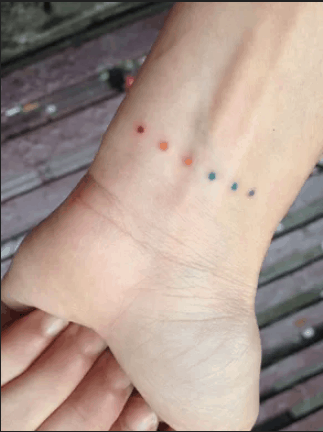 Small full color wrist tattoo of six dots: red, orange, yellow, green blue and purple.