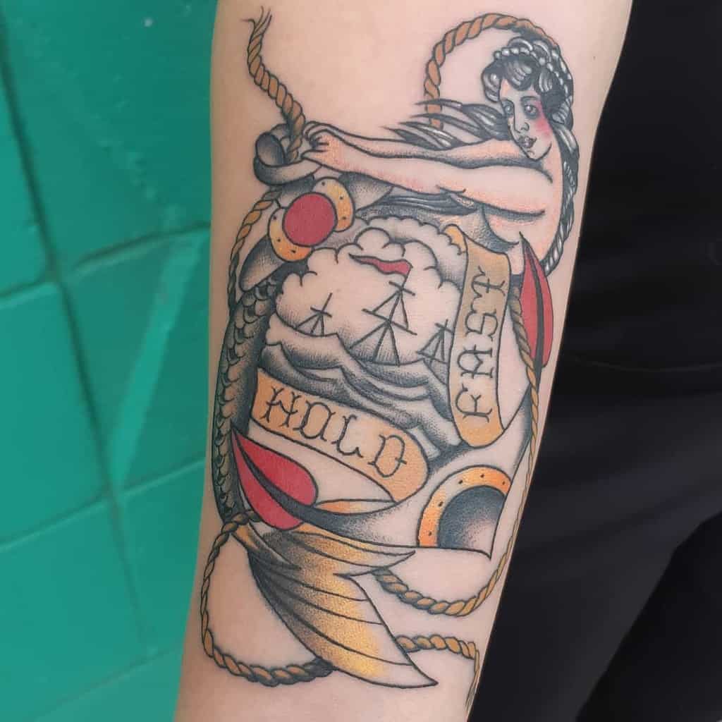 Tattoo of a sailor woman, ships, and a banner reading "HOLD FAST," complemented by an anchor to symbolize strength and courage from the navy, adorning an arm