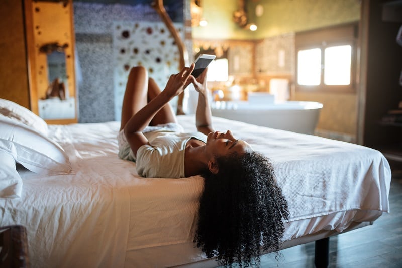 Woman Looking At Phone On Bed