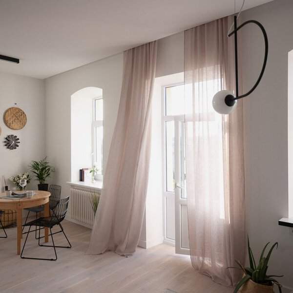Minimalist dining room with soft sheer curtains, a wooden table, and black metal chairs.