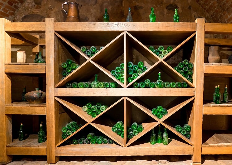 Rustic wine cellar with wooden shelves and green glass bottles arranged in a diagonal rack.