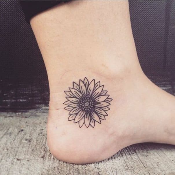medium-sized black line tattoo on woman's foot near heel of a sunflower