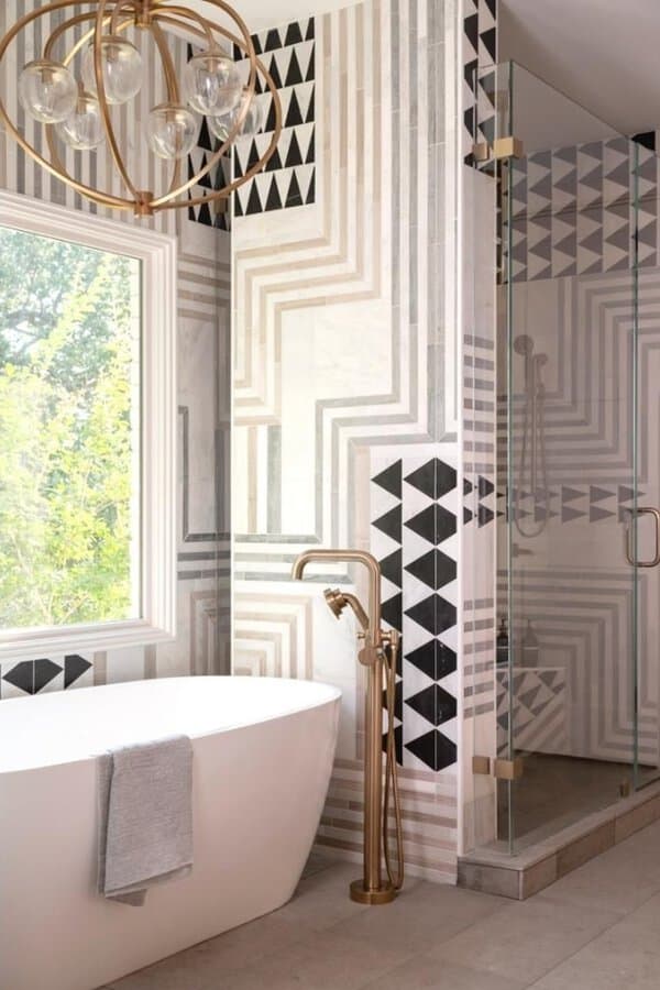 Gold orb chandelier above a white freestanding tub with bold geometric tile in a striking, contemporary bathroom.