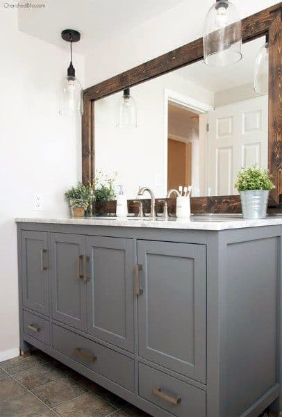 Bathroom with gray vanity, rustic wood-framed mirror, and hanging pendant lights.