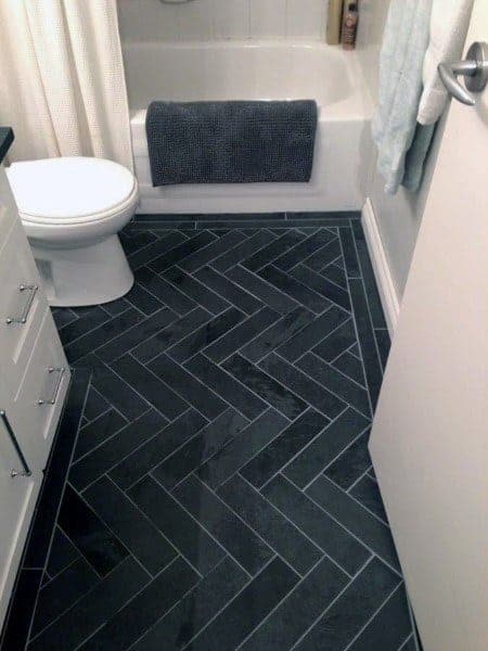 Bathroom with dark herringbone tile flooring, white fixtures, and a small tub.