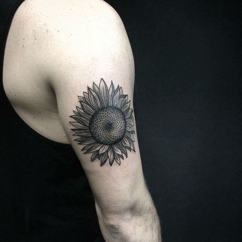 large black and grey tattoo on man's upper arm of a dark realistic sunflower