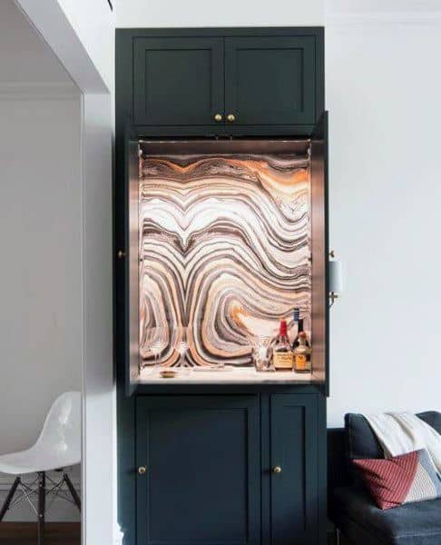 Chic mini bar with black cabinetry, illuminated marble-patterned backsplash, and elegant display.