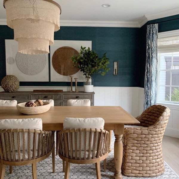 Boho dining room with a wooden table, woven chairs, layered textiles, and deep blue walls.