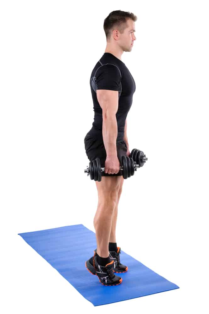 young man shows finishing position of standing dumbbell calf raise