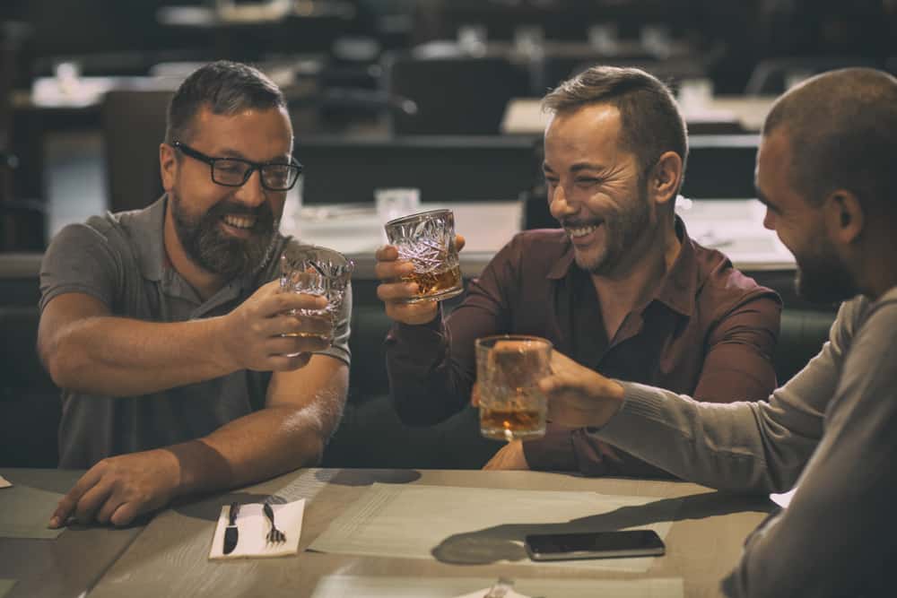 cheerful smiling men with glass of whiskey and friends 