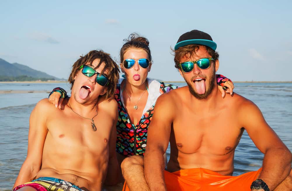 Two young men and a young woman sitting in water wearing colorful mirrored sunglasses