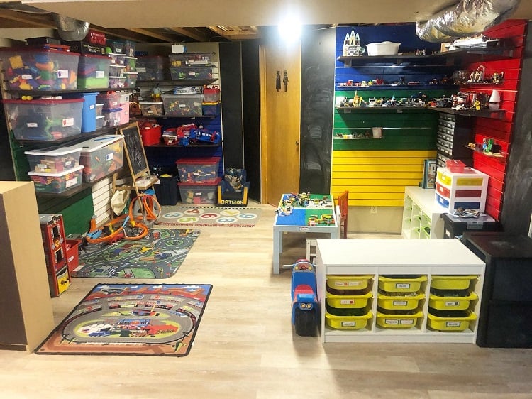 Colorful basement playroom with labeled storage bins, toys, and activity tables for kids.