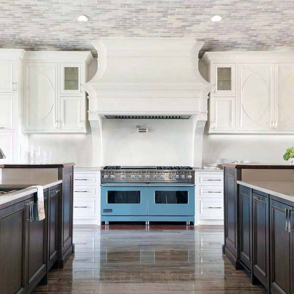 ornate kitchen with dual blue stoves and large white hood