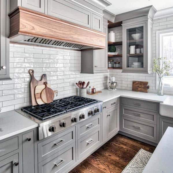 gray cabinet kitchen with wood hood and white tile backsplash 