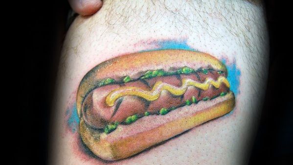Realistic hot dog tattoo featuring a sausage with mustard and relish inside a soft bun, with subtle color shading around it.