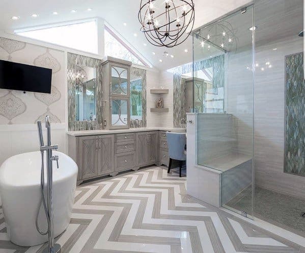 Luxury bathroom with freestanding tub, glass shower, gray chevron flooring, and chandelier lighting.