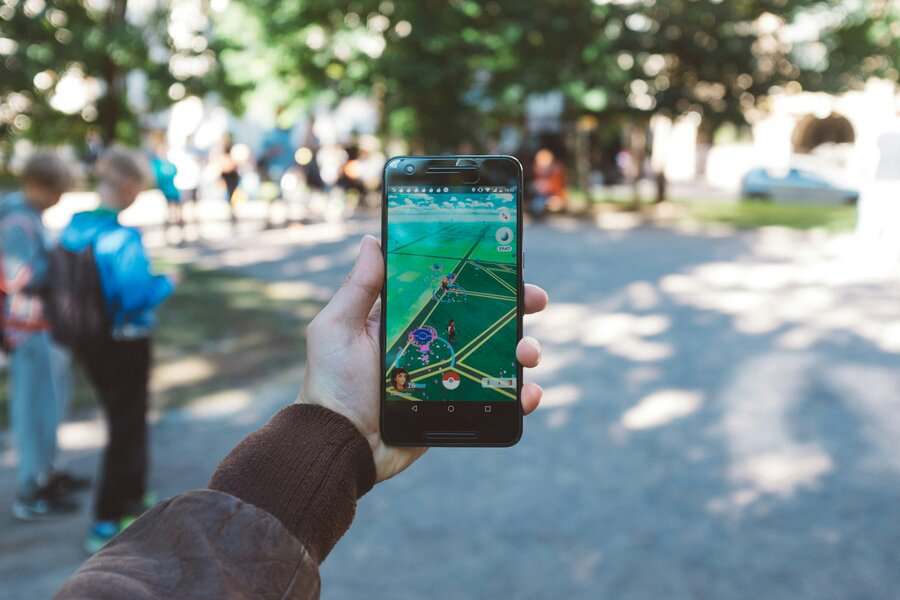 Someone playing Pokémon GO, a top mobile game, on their phone in a park with blurred people and trees in the background