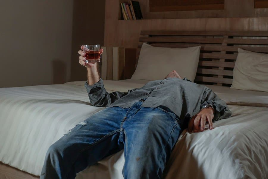 drunk man drinking whiskey glass at home lying on bed