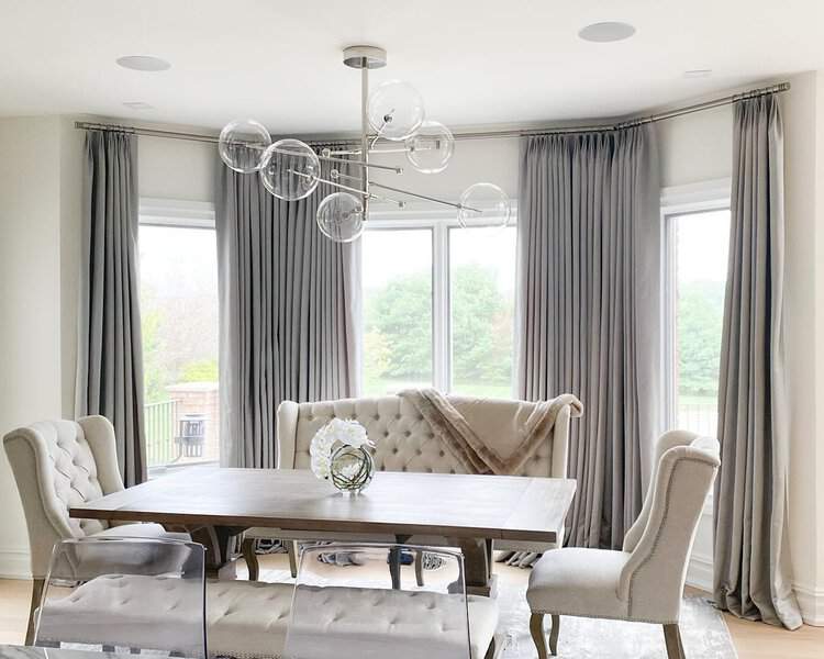 Elegant dining room with floor-length gray curtains, tufted chairs, and a stylish chandelier.