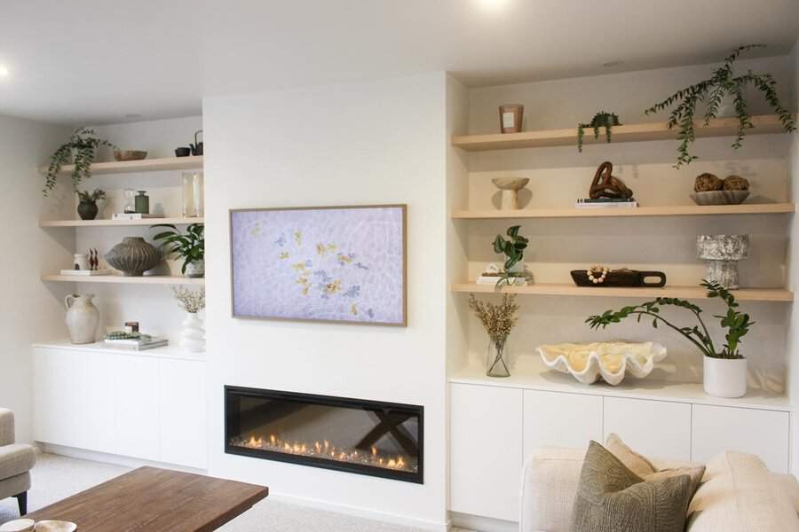 Minimalist living room with floating wooden shelves, a modern fireplace, and neutral decor.