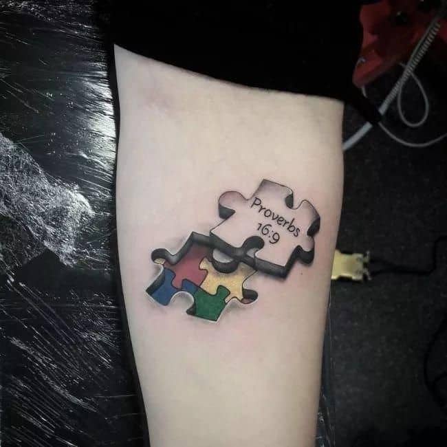 Full color forearm tattoo with black and gray puzzle piece revealing multi-colored puzzle pieces beneath with “Proverbs 16:9”.