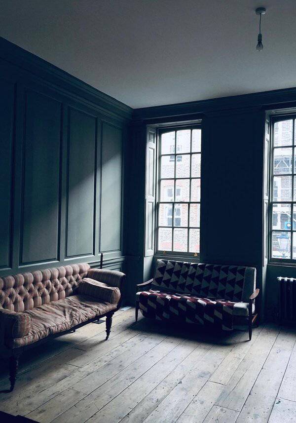 Moody Georgian room with deep paneling, tall windows, and two mismatched sofas for a quietly dramatic interior.