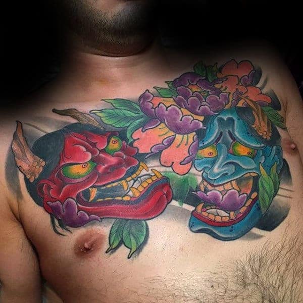 Vivid chest tattoo showcasing red and blue Hannya masks surrounded by colorful peonies, blending tradition and bold design
