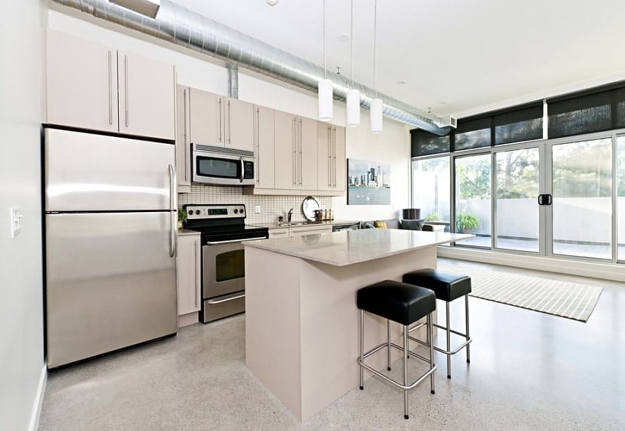 large industrial style kitchen concrete floor white cabinets two black stools 