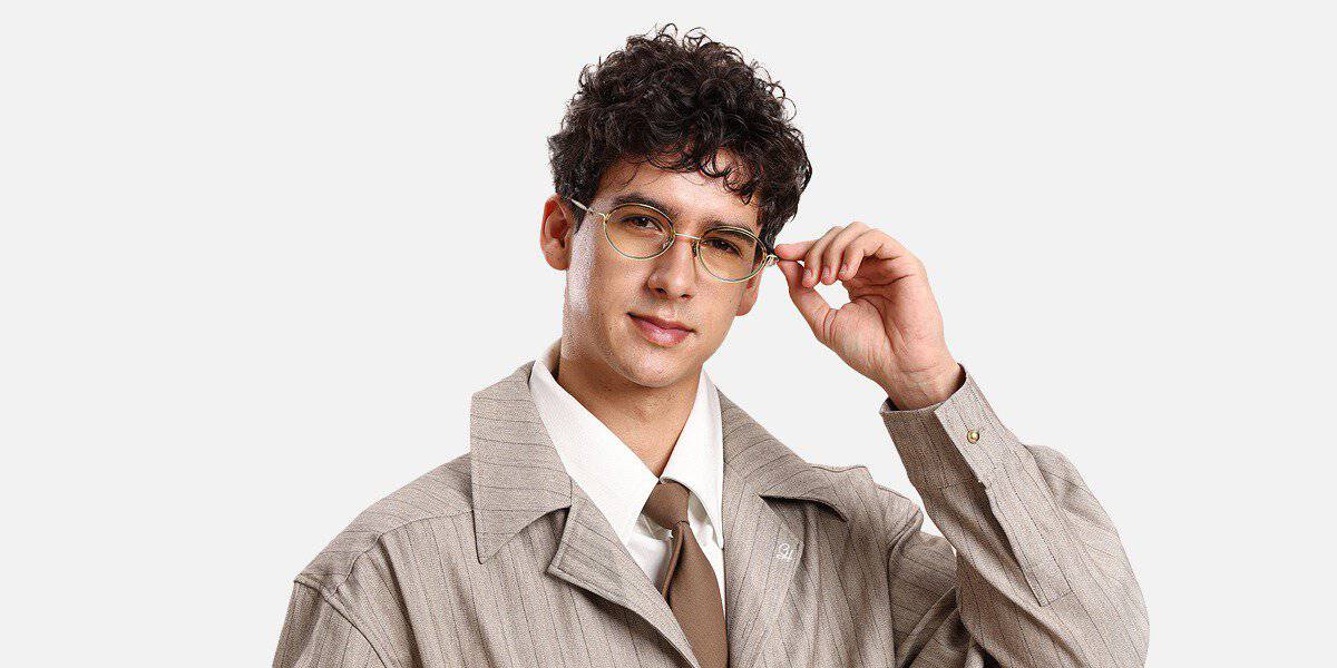 Man with curly hair in a beige suit adjusts his prescription lenses, facing the camera in modern, budget-friendly frames