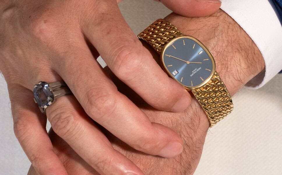 Two hands overlap; one wears a gold watch perfect for vintage collectors and the other sports a silver gemstone ring