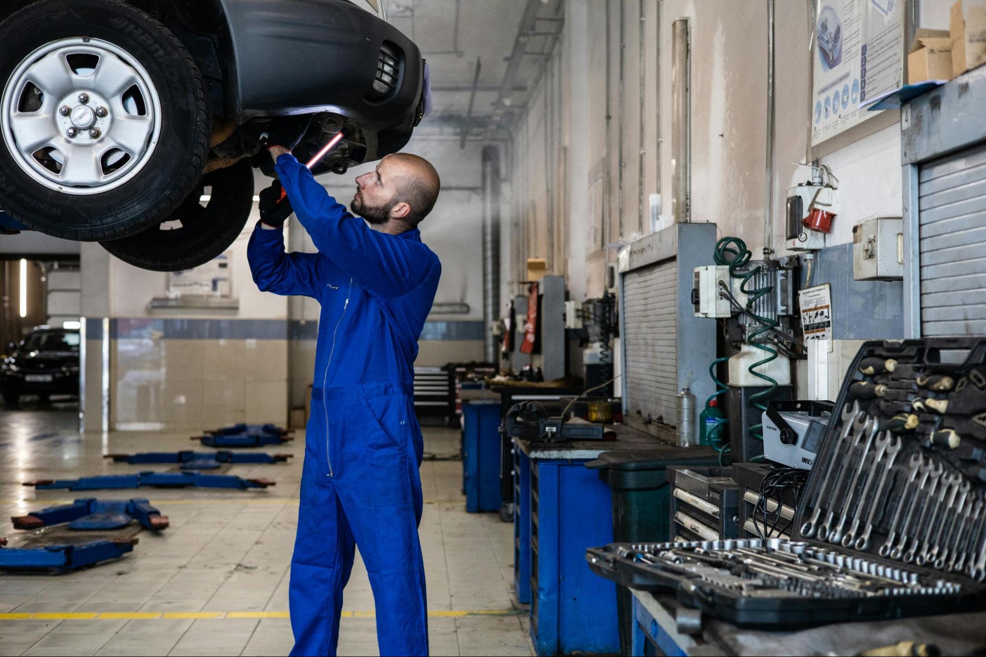 A mechanic in blue coveralls checks under a car, using OEM parts for top resale value at an auto repair shop